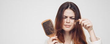 Kvinna som tittar på en hårborste fylld med tappat hår
